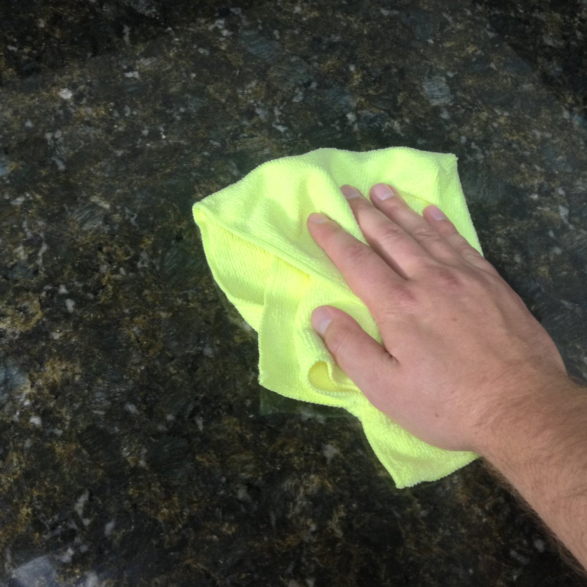 Green microfiber cleaning cloth wiping a dark countertop surface