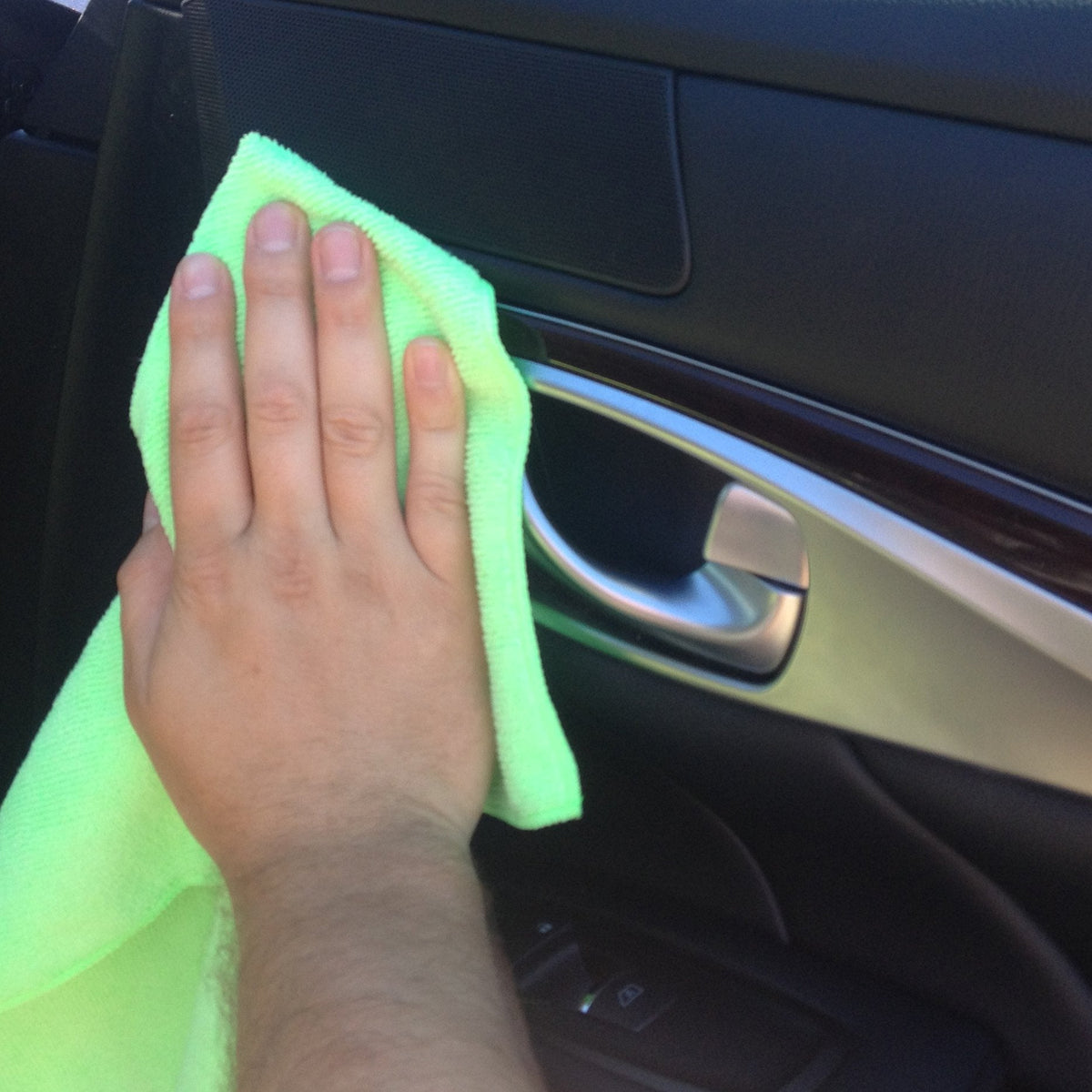 Green microfiber cleaning cloth wiping a car interior door panel